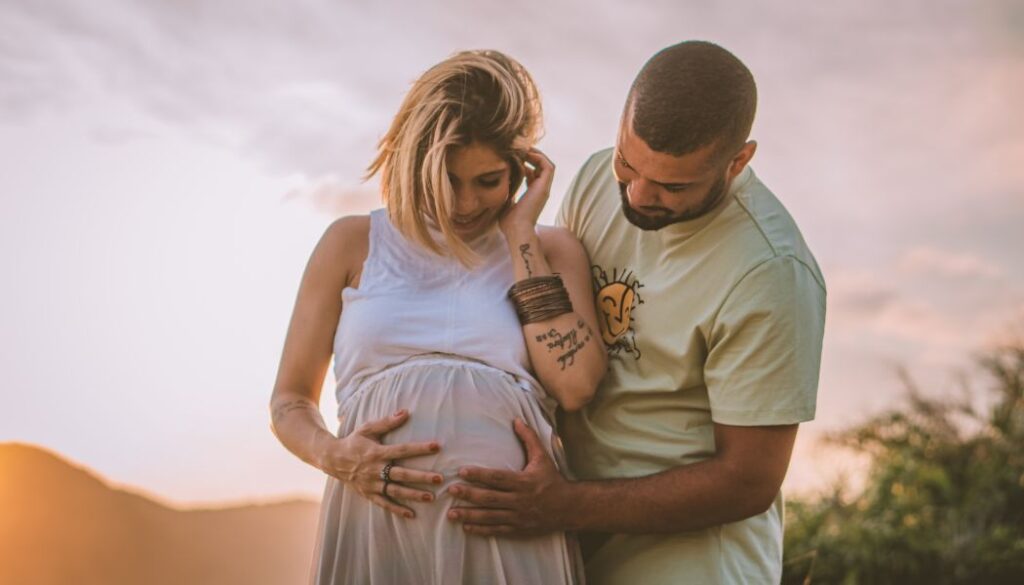 pregnant couple touching at the sunset