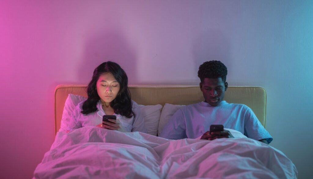 couple lying on bed scrolling phones