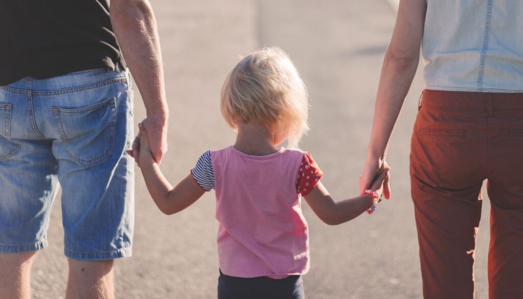 parents holding hands with a child from the back